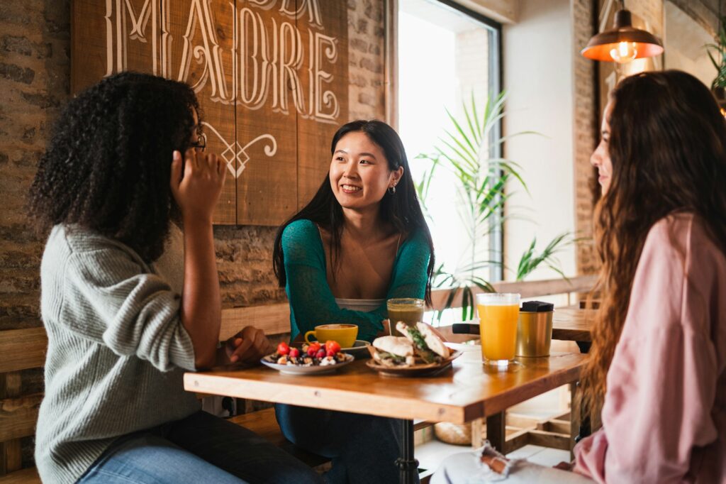 Three smiling friends gossiping while they are having brunch in a cafeteria